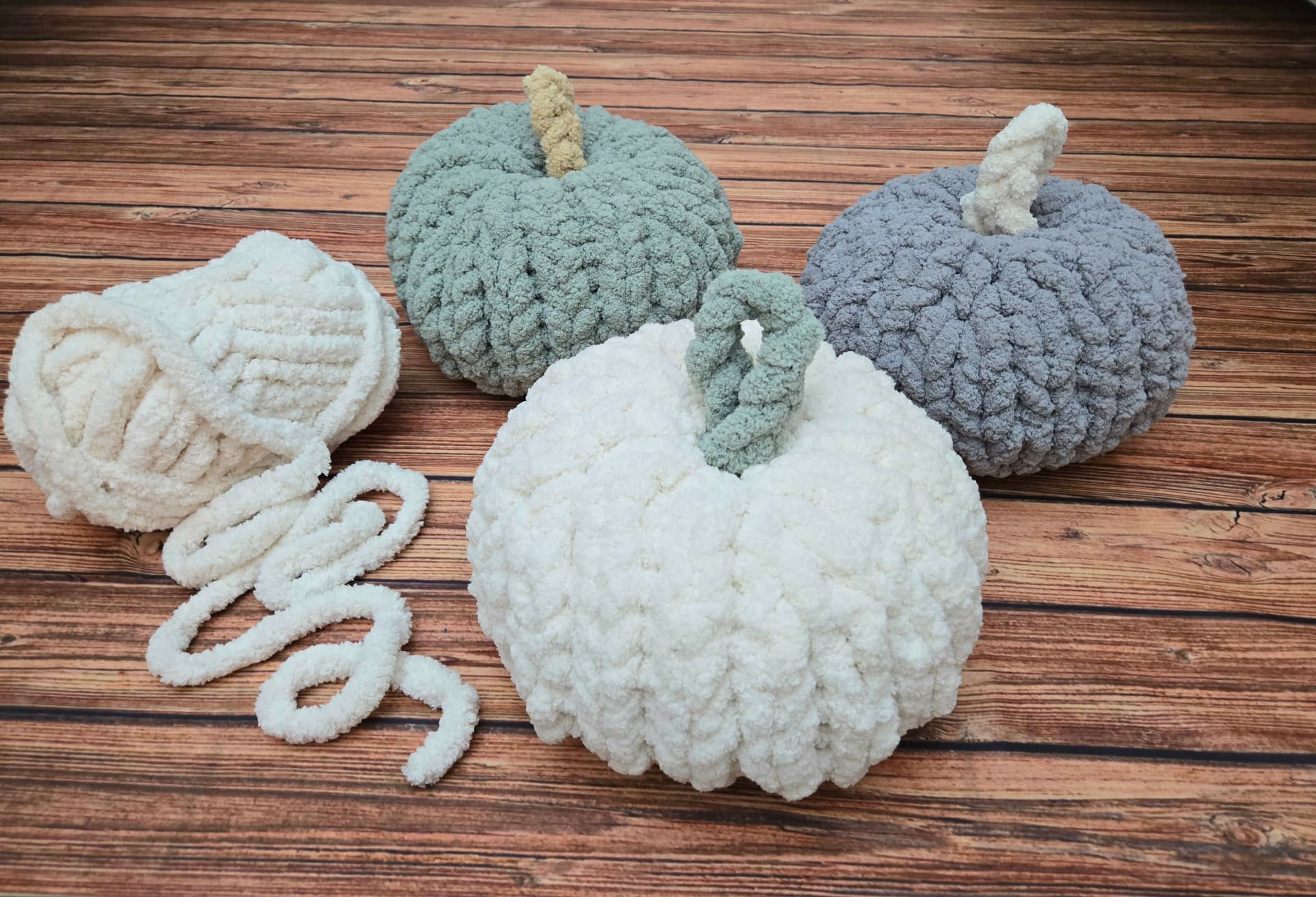 Chunky knit pumpkins in sage, cream, and grey yarn on a wooden table